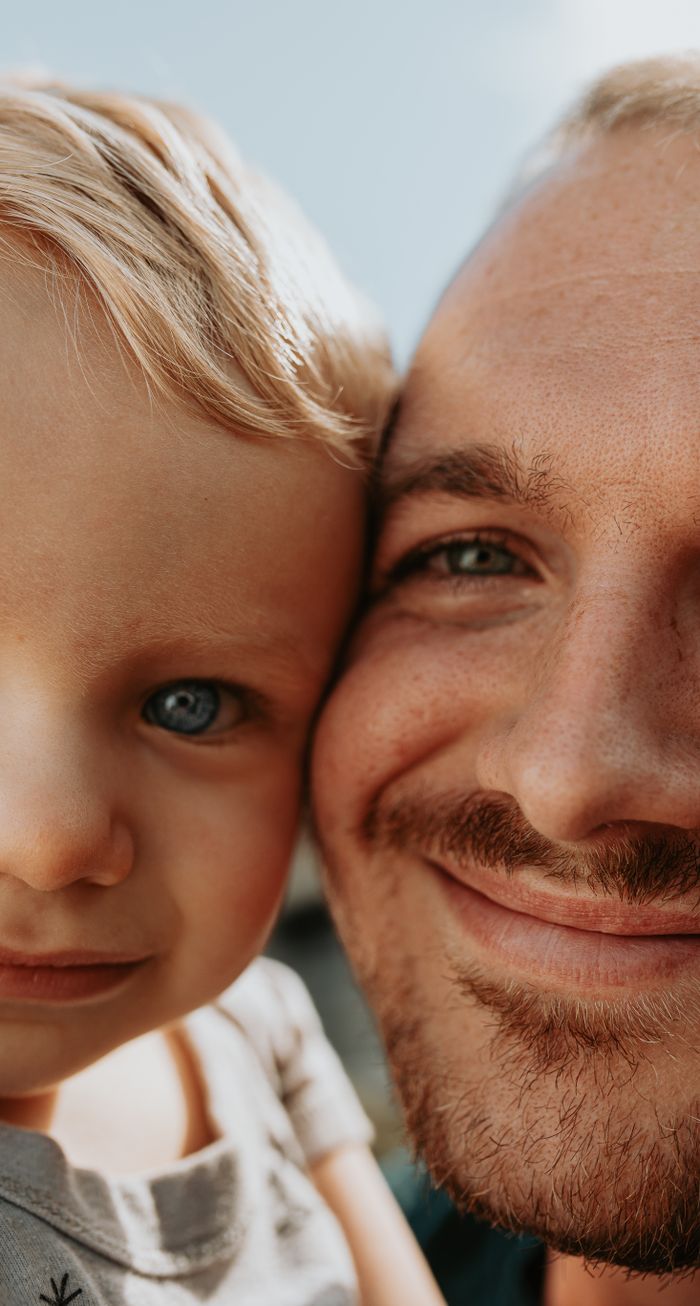 gallery-6 Close-up portrait of a smiling father and child enjoying a joyful moment together.