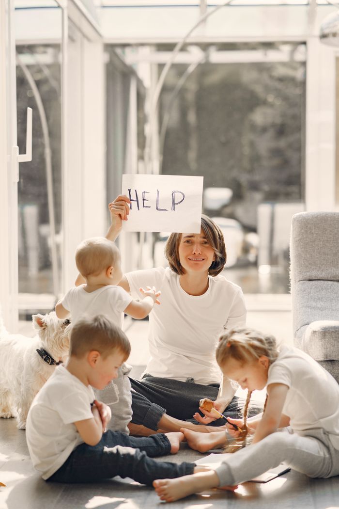 gallery-1 Woman holding placard with sign help while looking after children on floor in well lit living room