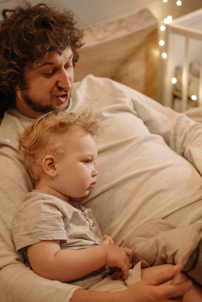 hero-img-02 A father and son reading together in a cozy bedroom setting, promoting family bonding.
